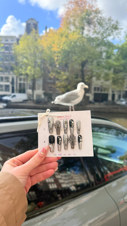 Person holding a card with nail art designs in front of a canal scene with a seagull.
